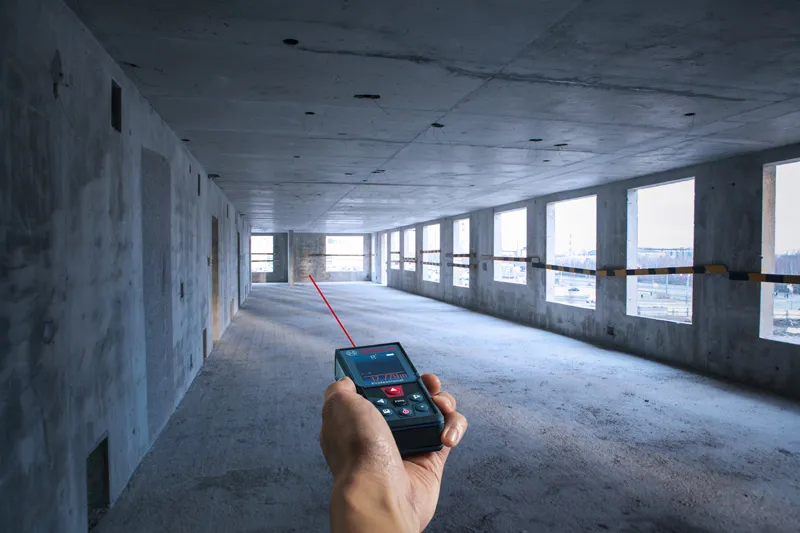 Người sử dụng máy đo laser để xác định khoảng cách trong một căn phòng bê tông chưa hoàn thiện.