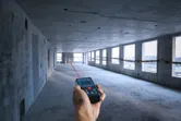 Người sử dụng máy đo laser để xác định khoảng cách trong một căn phòng bê tông chưa hoàn thiện.