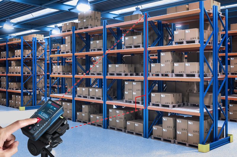 Một người sử dụng máy đo laser để kiểm tra khoảng cách giữa các kệ hàng trong kho.