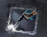 Một người mặc đồ bảo hộ đang sử dụng búa phá dỡ để phá vỡ bức tường bê tông.