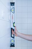 Người giữ một ống thủy dài 60cm thẳng đứng dựa vào bức tường lát gạch.
