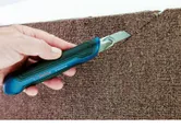 Một người dùng dao rọc giấy để cắt thảm dọc theo mép thảm.