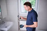 Một người sử dụng camera nhiệt và điện thoại thông minh trong phòng tắm lát gạch.