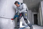 Một người mặc đồ bảo hộ đang khoan vào bức tường bê tông trong khu vực đang thi công.