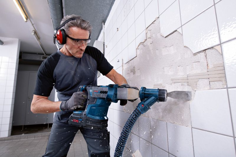 GBH 18V-34 CF Một người mặc đồ bảo hộ đang dùng búa quay không dây để tháo gạch ốp tường.