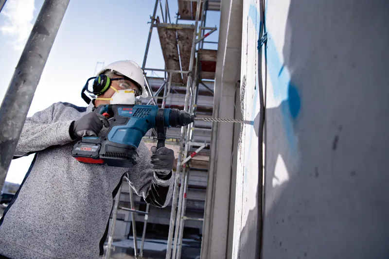 Một người đàn ông mặc đồ bảo hộ đang khoan vào bức tường bê tông tại một công trường xây dựng.