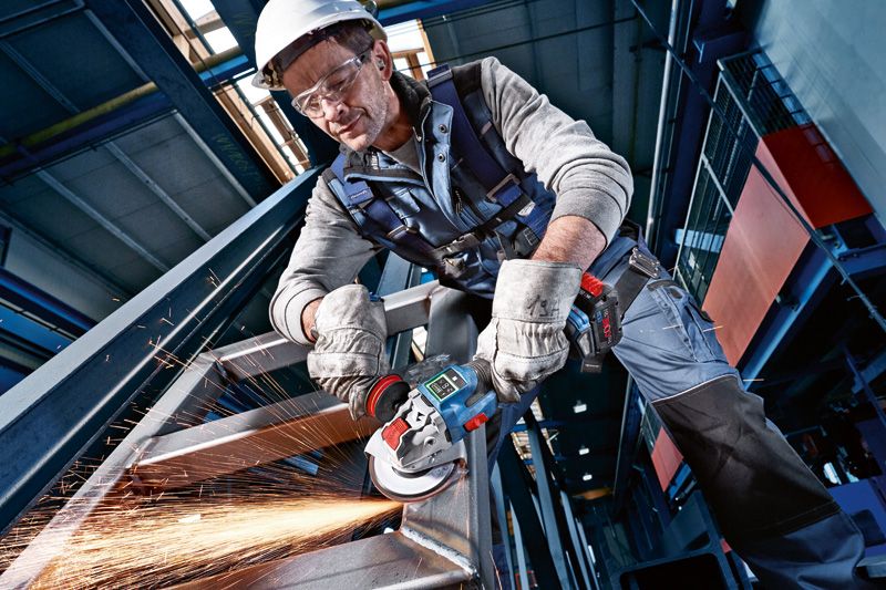 Một người mặc đồ bảo hộ dùng dụng cụ điện mài một thanh kim loại, tạo ra tia lửa.