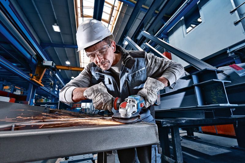 Một người đeo thiết bị an toàn đang mài kim loại bằng máy mài góc không dây.