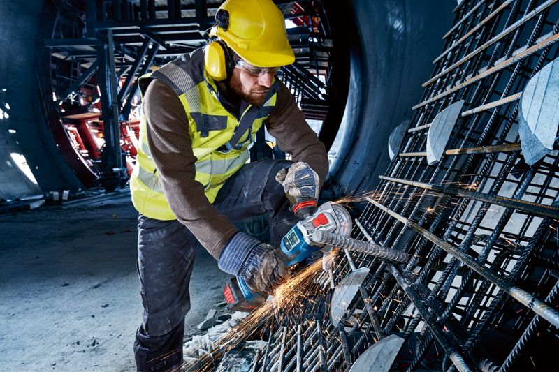 Một người đeo thiết bị an toàn sử dụng máy mài góc không dây để cắt cốt thép.