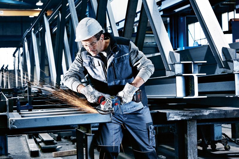 Một người mặc đồ bảo hộ đang mài các thanh kim loại bằng máy mài góc không dây.