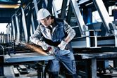 Một người mặc đồ bảo hộ đang mài các thanh kim loại bằng máy mài góc không dây.