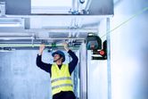 Một người mặc thiết bị an toàn đang căn chỉnh các đường ống bằng dụng cụ cân bằng laser màu xanh lá cây.