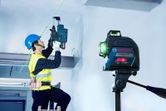 Một người mặc đồ bảo hộ đang khoan trần nhà theo hướng dẫn của máy cân bằng laser.