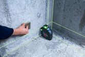 Người đang sử dụng khối chà nhám trên tường bê tông, bên cạnh một công cụ cân bằng laser đang hoạt động.