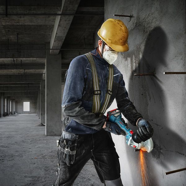 GWS 180-LI Một người mặc đồ bảo hộ đang cắt bê tông bằng máy mài góc.