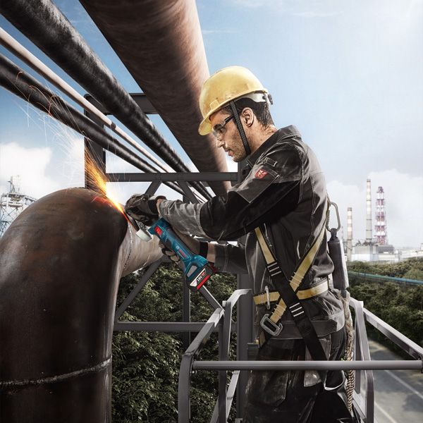 Một người mặc đồ bảo hộ đang mài một ống kim loại lớn bằng máy mài góc.