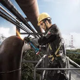Một người mặc đồ bảo hộ đang mài một ống kim loại lớn bằng máy mài góc.