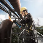 Một người mặc đồ bảo hộ đang mài một ống kim loại lớn bằng máy mài góc.