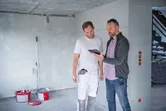 Hai người xem xét bản thiết kế xây dựng trên máy tính bảng, một người cầm thiết bị đo kỹ thuật số.