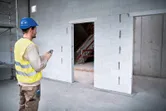 Người đeo thiết bị an toàn sử dụng máy đo laser để kiểm tra kích thước cửa ra vào tại công trường xây dựng.
