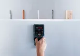 Một người đang quét tường thạch cao bằng máy dò, xác định các đường ống và dây điện ẩn.