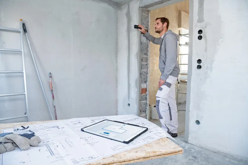 Một người sử dụng máy đo laser để kiểm tra khoảng cách tường tại công trường xây dựng.