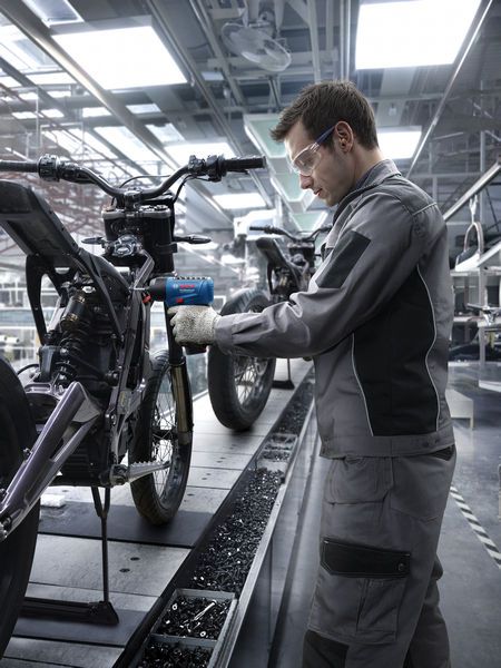 Một người mặc đồ bảo hộ đang sử dụng dụng cụ điện để lắp ráp khung xe máy.