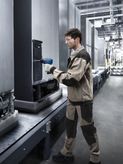 Một người mặc thiết bị an toàn đang sử dụng dụng cụ điện để kiểm tra thiết bị trên dây chuyền lắp ráp.