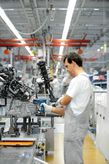 Người đeo thiết bị an toàn sử dụng dụng cụ điện để lắp ráp máy móc trên dây chuyền sản xuất.