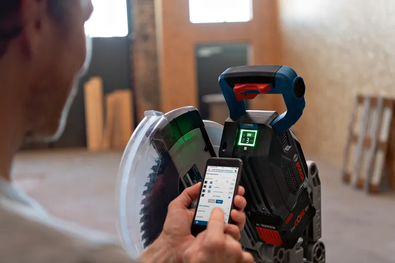 Một người đang điều chỉnh máy cưa cắt góc không dây bằng ứng dụng trên điện thoại thông minh.