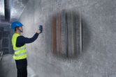 Một người mặc thiết bị an toàn sử dụng máy dò trên tường bê tông để xác định đường ống ẩn.