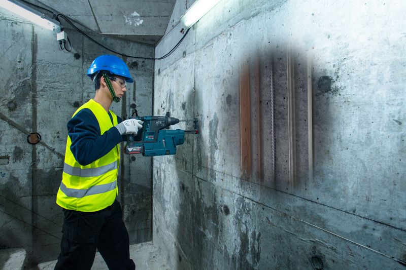 Một người mặc thiết bị an toàn đang quét bức tường bê tông bằng máy dò, phát hiện ra các đường ống bên trong.