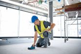 Một người mặc đồ bảo hộ đang quét sàn của công trường xây dựng bằng máy quét tường.