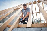 Một người mặc thiết bị an toàn sử dụng cờ lê lực không dây để siết chặt các thanh gỗ.