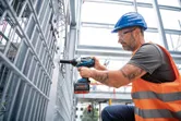 Một người mặc thiết bị an toàn đang sử dụng cờ lê lực không dây để mở hàng rào kim loại.
