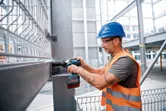 Một người mặc thiết bị an toàn đang sử dụng cờ lê tác động không dây trên một thanh thép.
