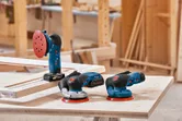 Ba máy chà nhám điện đặt trên một chiếc bàn làm việc bằng gỗ trong một xưởng mộc.