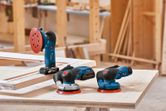 Ba máy chà nhám điện đặt trên một chiếc bàn làm việc bằng gỗ trong một xưởng mộc.