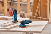 Máy chà nhám quỹ đạo ngẫu nhiên không dây được đặt trên bàn làm việc bằng gỗ trong xưởng mộc.