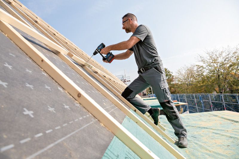 Một người mặc thiết bị an toàn sử dụng máy khoan không dây để đóng gỗ trên mái dốc.