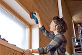 Một người mặc đồ bảo hộ đang chà nhám khung cửa sổ bằng gỗ bằng máy chà nhám quỹ đạo ngẫu nhiên không dây.