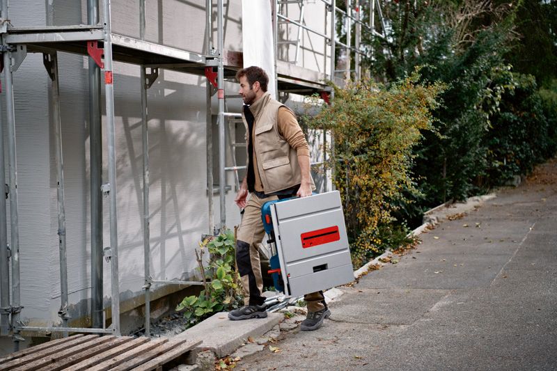 Một người mặc đồ bảo hộ đang mang theo máy cưa bàn không dây tại công trường xây dựng.