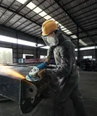 Một người mặc đồ bảo hộ đang mài kim loại bằng dụng cụ điện trong nhà máy.