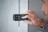Người đo khoảng cách tường bằng thước đo laser, thấy rõ màu sơn trên tay họ.
