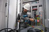 Một người mặc thiết bị an toàn sử dụng súng nhiệt không dây trên hệ thống dây điện.