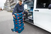 Một người đang chất các hộp dụng cụ xếp chồng lên nhau lên xe đẩy bên cạnh một chiếc xe tải làm việc mở.