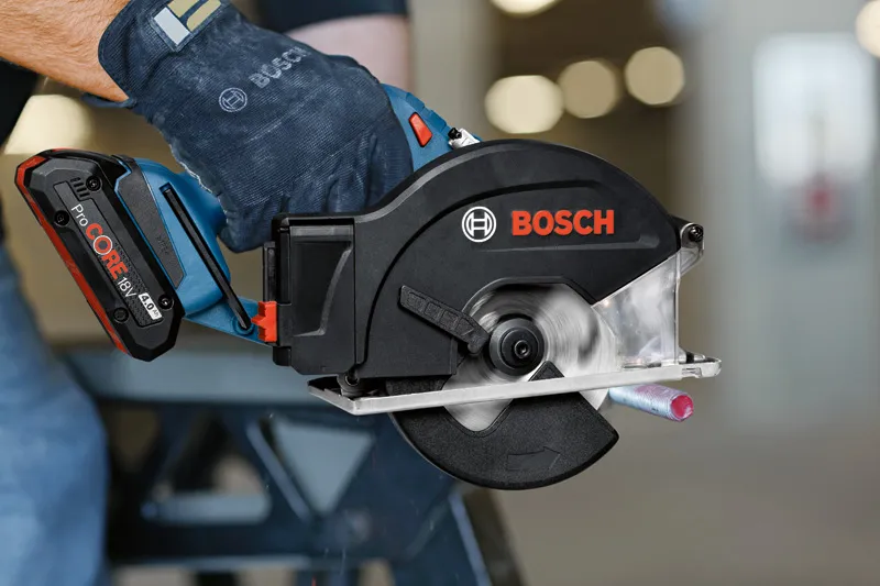GKM 18V-50 Một người mặc đồ bảo hộ đang cắt một ống kim loại bằng máy cưa tròn không dây.