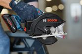 Một người mặc đồ bảo hộ đang cắt một ống kim loại bằng máy cưa tròn không dây.