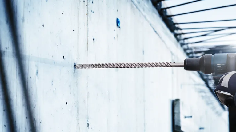 Mũi khoan búa EXPERT SDS max-8X 12 x 200 x 340 mm Người mặc đồ bảo hộ khoan vào tường bê tông bằng búa quay.