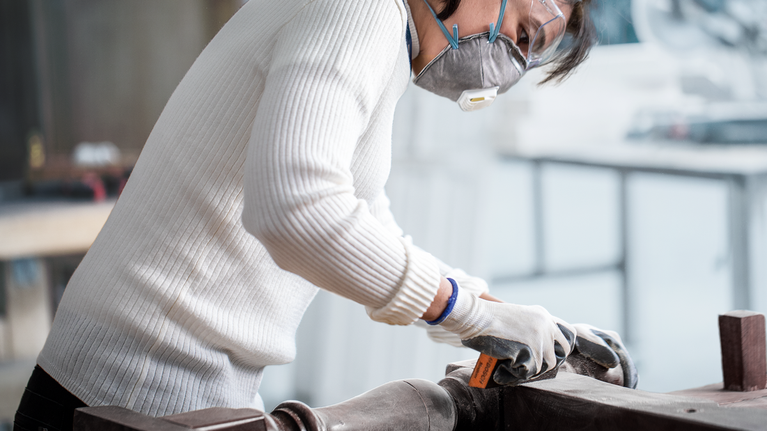 Người mặc đồ bảo hộ đang chà nhám bề mặt kim loại trong xưởng.